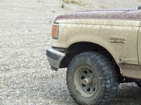 1990 Ford Bronco - Mud-covered 1990 Ford Bronco front quarter panel and tire on a gravel surface.