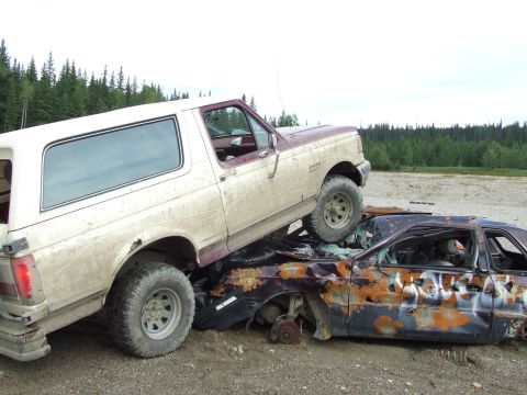 1990 Ford Bronco - A tan and maroon 1990 Ford Bronco is parked on top of a heavily damaged and rusted car.