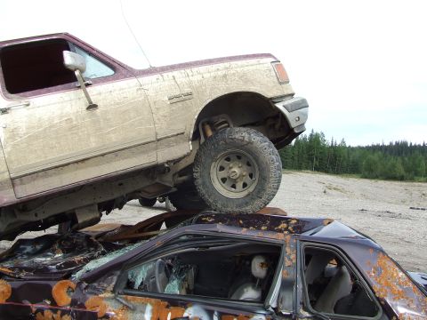 1990 Ford Bronco - A Ford Bronco is parked on top of a wrecked car in a junkyard.