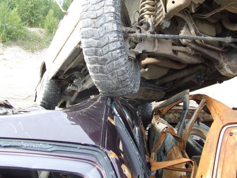 1990 Ford Bronco - Multiple wrecked vehicles are piled on top of each other, with one vehicle's undercarriage visible and another showing extensive fire damag…