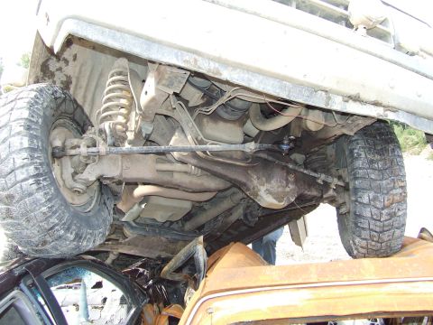 1990 Ford Bronco - Undercarriage of a vehicle is visible, resting on another damaged vehicle.