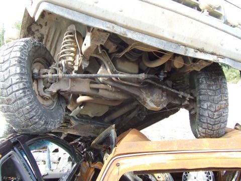 1990 Ford Bronco - The undercarriage of a vehicle is visible, with its tires resting on the roof of a damaged car.