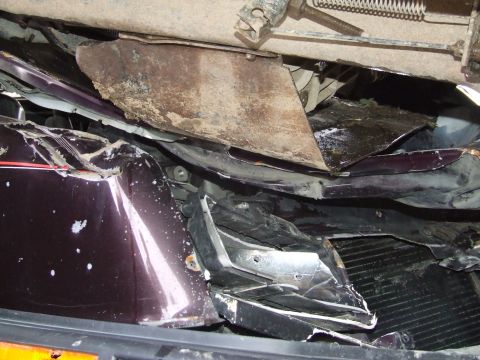 1990 Ford Bronco - The front end of a dark purple vehicle is heavily damaged, with bent metal and exposed components visible.