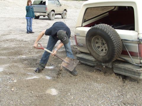 1990 Ford Bronco - A man digs mud from around a stuck Ford Bronco while another person watches.