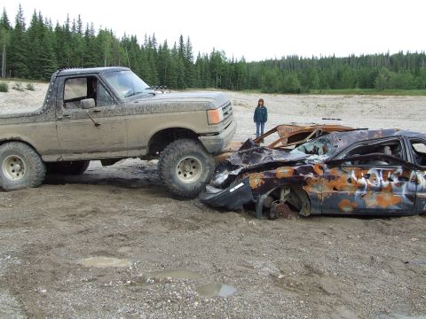 1990 Ford Bronco - A muddy 1990 Ford Bronco is parked next to a heavily damaged and rusted car in an outdoor setting.