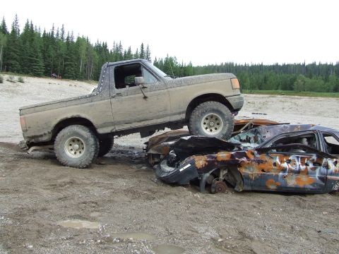 1990 Ford Bronco - A muddy 1992 Ford Bronco is driven over two destroyed vehicles in a junkyard.