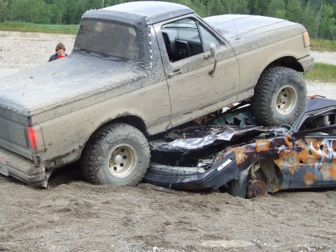 1990 Ford Bronco - A tan 1990 Ford Bronco is positioned on top of a heavily damaged and rusted car.
