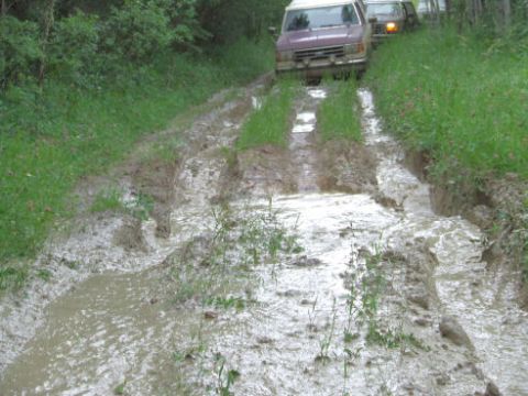 1988 Ford Bronco - Two SUVs navigate a challenging muddy path during an off-road excursion.