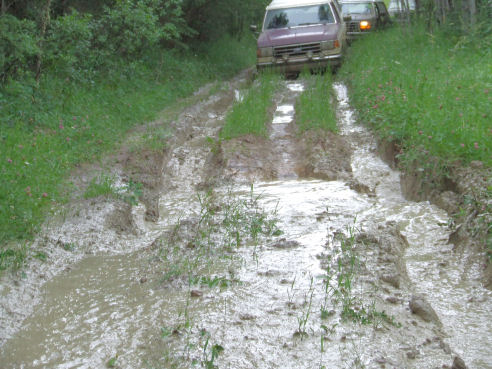 1988 Ford Bronco and another SUV driving on a muddy trail