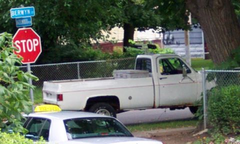 1978 Ford Bronco - A white pickup truck is parked on the side of the road, with a taxi visible in front of it.