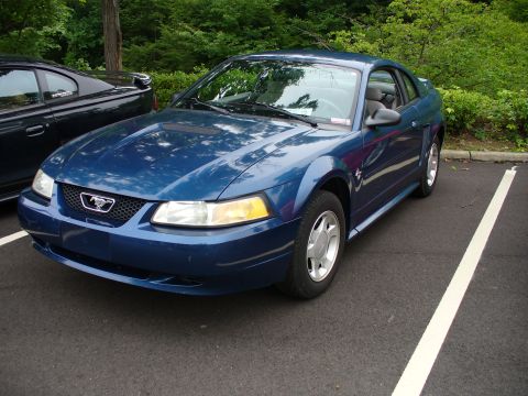 1991 Ford Probe - A blue Ford Mustang is parked in a lot, with another car visible to its left.