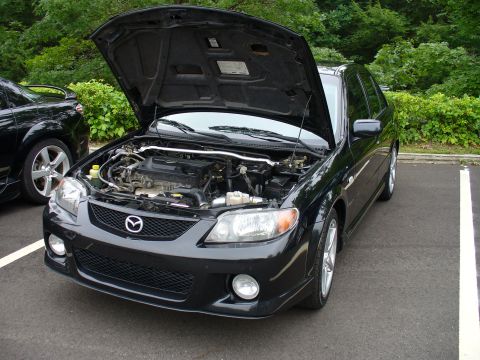 1991 Ford Probe - Front view of a black Mazda Protege with its hood open, parked in a lot.