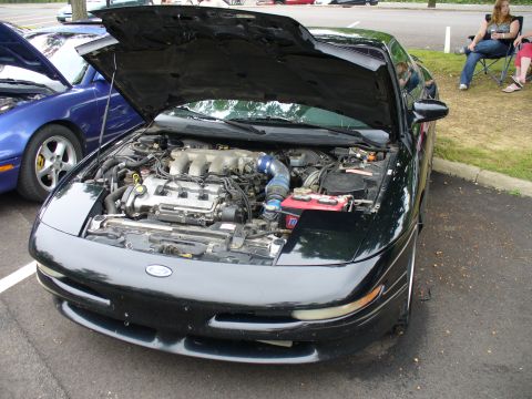 1991 Ford Probe - The engine bay of a black 1991 Ford Probe is displayed with the hood open, parked next to a blue car.