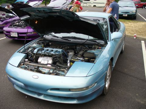 1991 Ford Probe - A light blue 1991 Ford Probe is displayed with its hood open, revealing the engine bay. Another purple car is visible behind it.