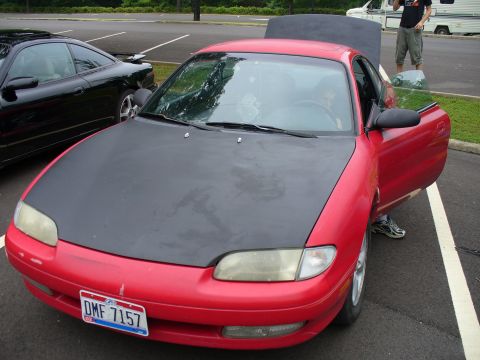 1991 Ford Probe - A red coupe with a matte black hood is parked in a lot, with the driver's door open.