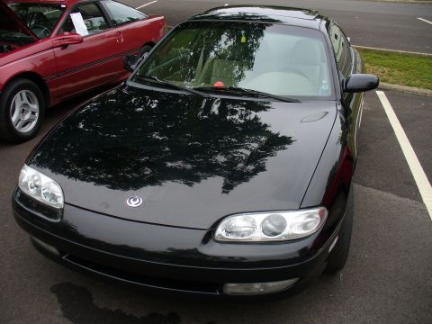 1991 Ford Probe - Front view of a black coupe parked next to a red car. The emblem on the hood is circular.