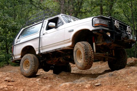 1996 Ford Bronco - Modified white Ford Bronco navigates challenging off-road terrain with one wheel lifted.