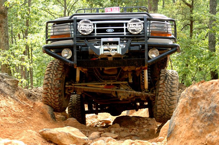 Ford Bronco with winch and brush guard navigating rocky terrain. "FOR SALE" sign visible on roof