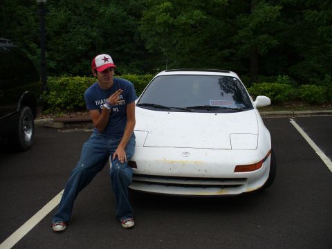 1991 Ford Probe - A person poses next to a white Toyota MR2, parked in a lot with trees in the background.