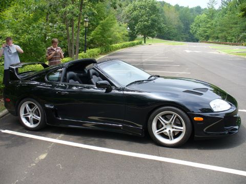 1991 Ford Probe - A black sports car with a distinctive rear spoiler and multi-spoke wheels is parked in an empty lot.
