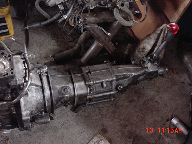 Manual transmission and transfer case assembly with red shifter knob on a garage floor