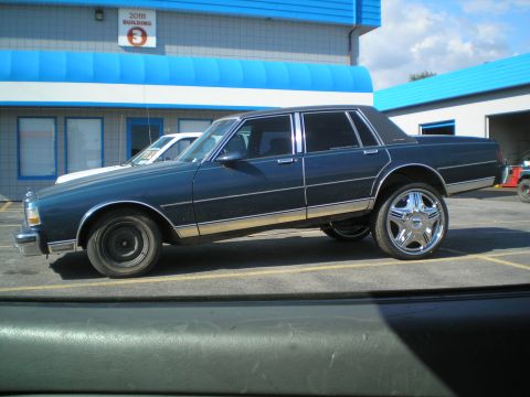 1985 Ford Bronco II - Side view of a modified sedan with large chrome wheels parked outside a building.