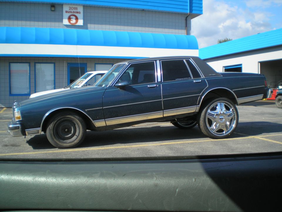 Dark blue sedan with chrome rims parked in a lot, another white vehicle behind it