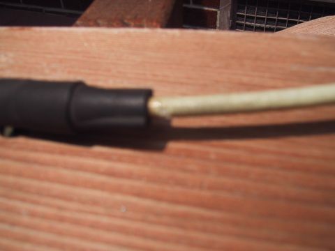 1994 Ford Bronco - An electrical wire with black insulation and a partially exposed conductor rests on a wooden surface.