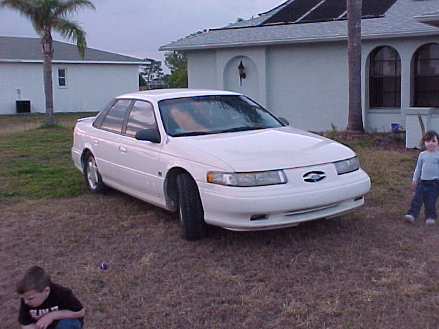 White 1994 Ford Taurus sedan parked on a grassy lawn in front of a house