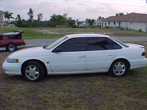 1994 Ford Taurus - Side view of a white 1994 Ford Taurus parked on grass with another car in the background.