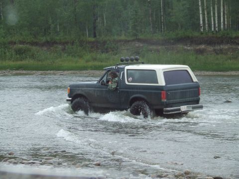 1990 Ford Bronco - A dark green and white 1990 Ford Bronco navigates through a shallow river.