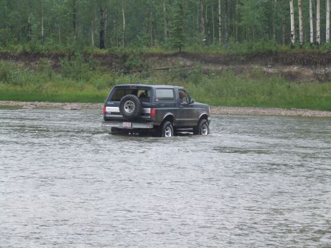 1990 Ford Bronco - A Ford Bronco navigates a river, its rear end visible as it drives through the water.