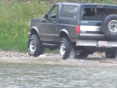 1990 Ford Bronco - A dark green 1990 Ford Bronco is seen driving through shallow water, with its rear visible.