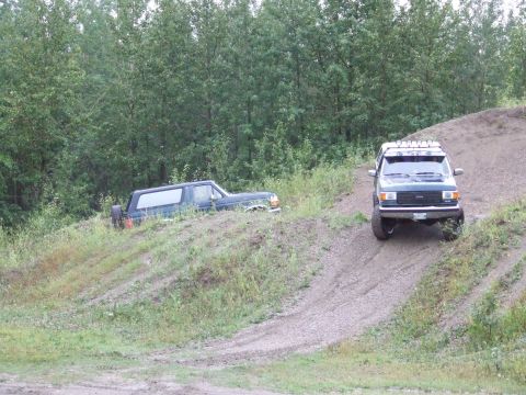 1990 Ford Bronco - Two SUVs navigate a dirt hill, one ascending and the other partially obscured on the slope.
