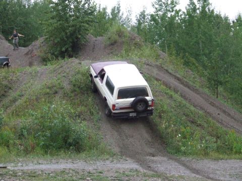 1990 Ford Bronco - A 1990 Ford Bronco navigates a steep dirt incline, with a person observing from a nearby mound of gravel.