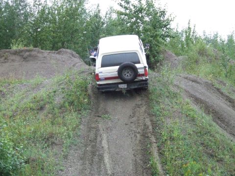 1990 Ford Bronco - White 1990 Ford Bronco navigates a steep dirt incline, spare tire mounted on the rear door.