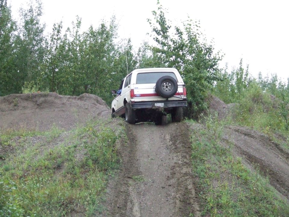 White 1990 Ford Bronco climbing a steep dirt hill with trees in the background
