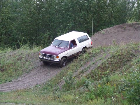 1990 Ford Bronco - This two-tone Ford Bronco navigates a challenging off-road terrain with dense trees in the background.