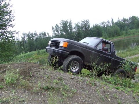 1990 Ford Bronco - A black 1990 Ford Bronco navigates a steep dirt incline with a body of water in the background.