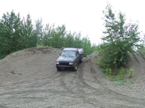 1990 Ford Bronco - A black 1990 Ford Bronco navigates a steep gravel incline amidst trees.