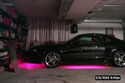 2001 Ford Mustang - A black coupe with pink underglow is parked in a garage, showing off its custom wheels and side profile.