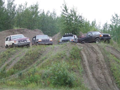 1990 Ford Bronco - Several off-road vehicles navigate a challenging dirt terrain under an overcast sky.