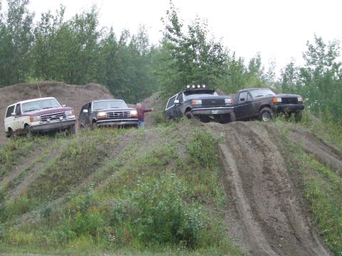 1990 Ford Bronco - Several Ford Broncos and a van are seen on a dirt hill in a wooded area.