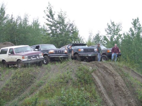 1990 Ford Bronco - Four Ford Broncos are parked on a dirt hill, with trees in the background.