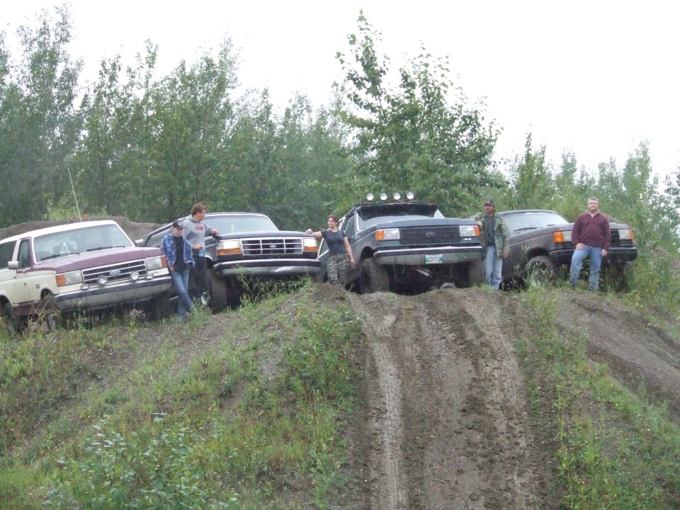 Group of people with several trucks and SUVs on a muddy hill