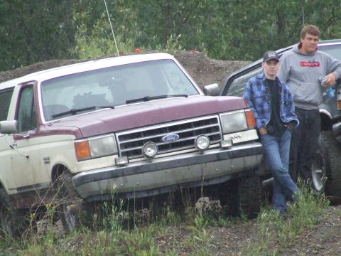 1990 Ford Bronco - A maroon and white Ford Bronco is parked off-road with two men standing nearby.
