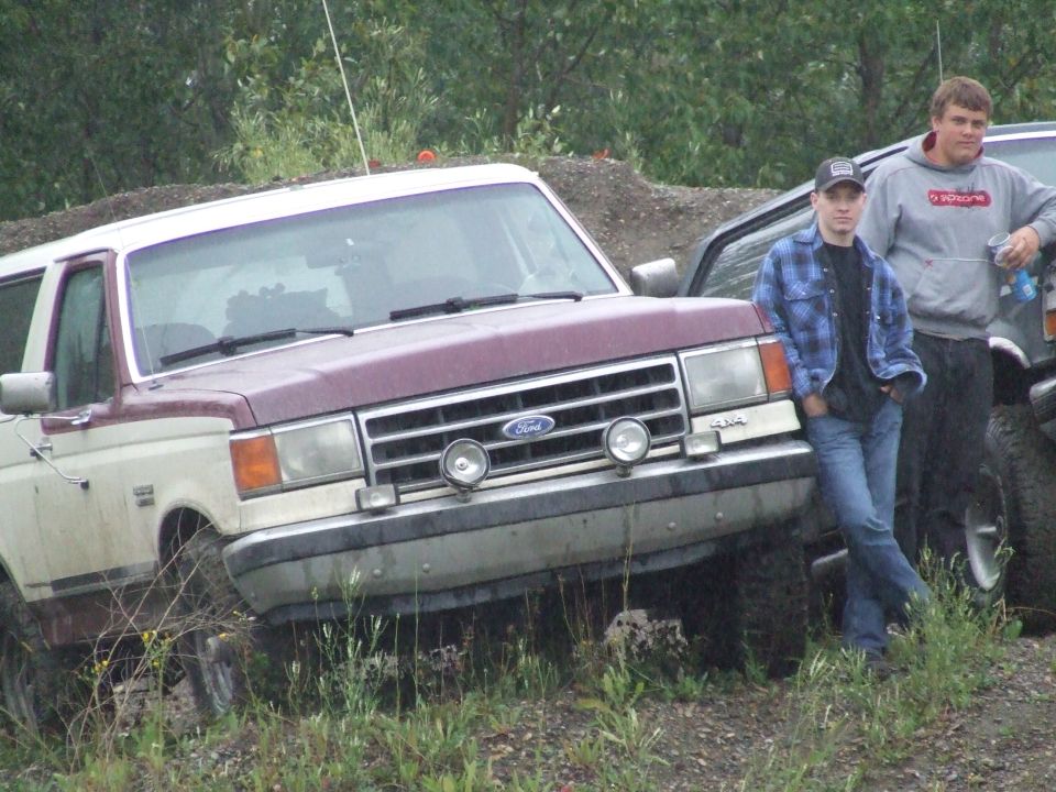 Maroon and white Ford Bronco with a chrome grille and two round fog lights, parked off-road