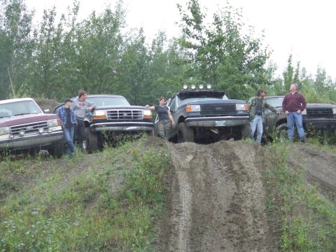 1990 Ford Bronco - Several Ford Broncos are gathered off-road, with people standing around them on a dirt embankment.
