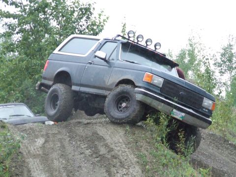 1990 Ford Bronco - This modified Ford Bronco is navigating a challenging off-road course, with another vehicle stuck in the mud.
