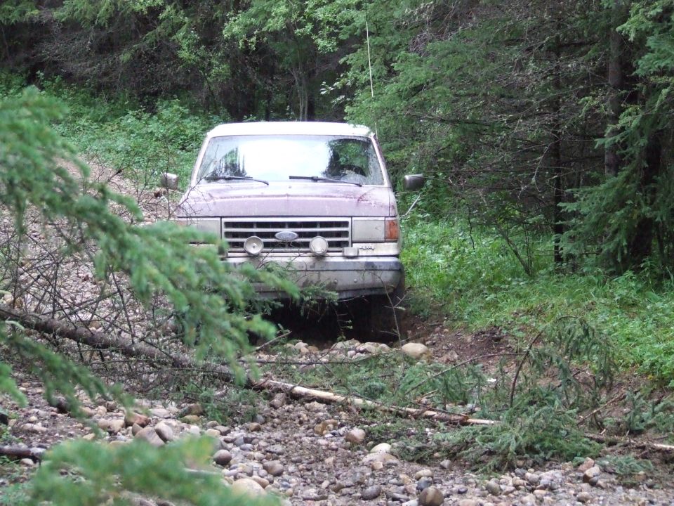 Front view of a maroon Ford Bronco on a rocky, wooded trail